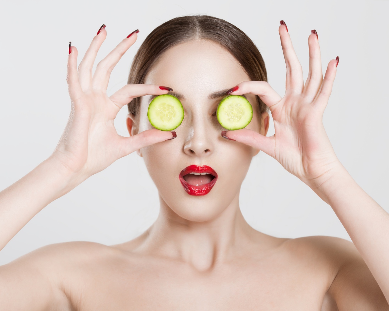 Яркая девушка с огурцами у глаз на сером фоне