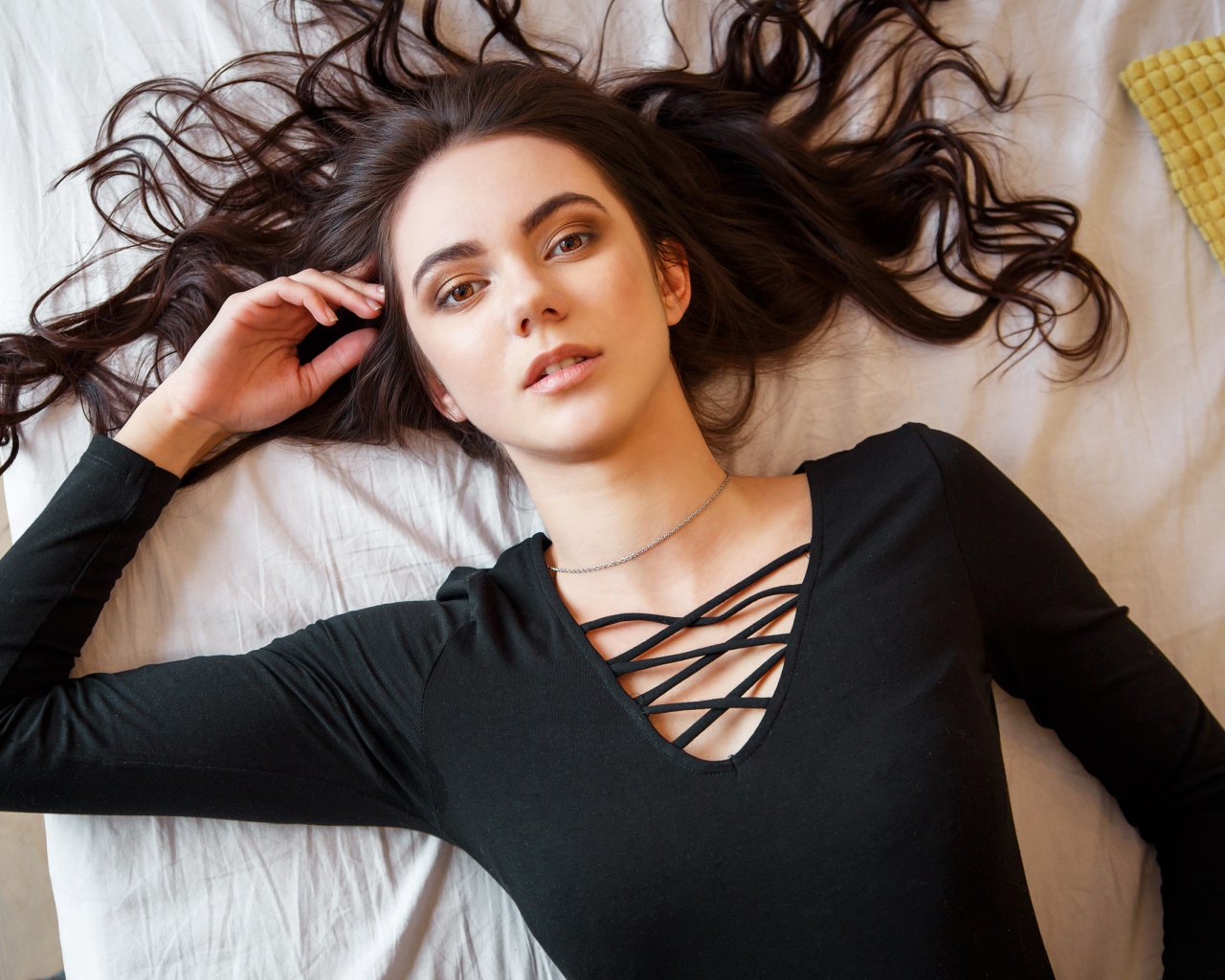 Кареглазая девушка в черном лежит на кровати