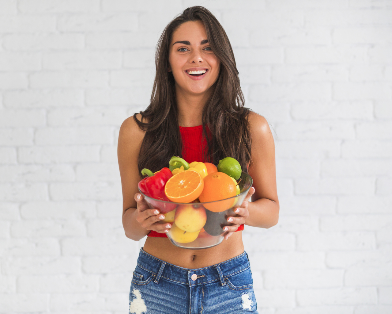 Брюнетка с миской фруктов на фоне стены