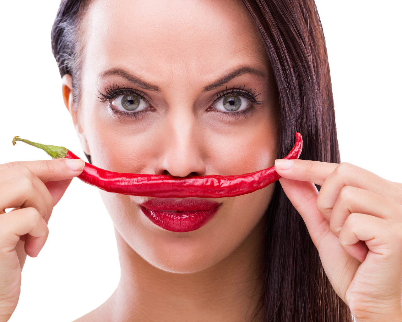 Брюнетка с красным перцем у лица на белом фоне
