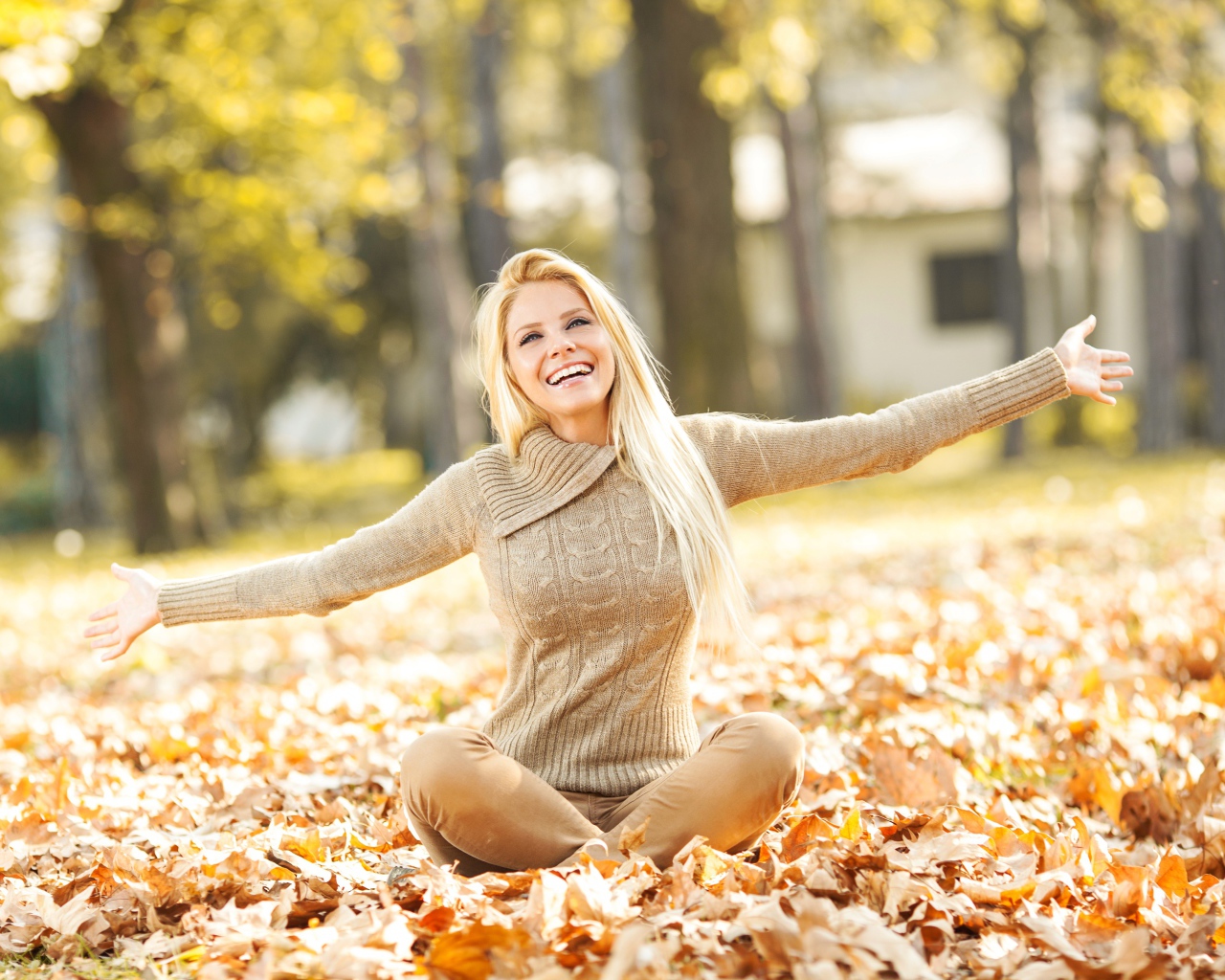 Веселая девушка сидит на опавшей листве осенью 