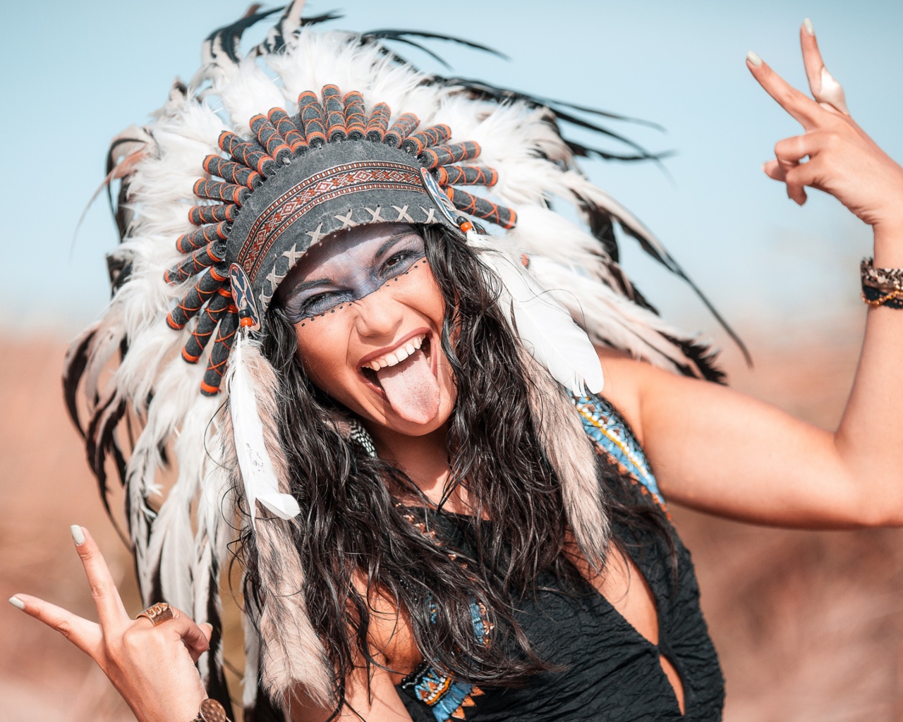 Веселая девушка с высунутым языком в костюме индейца