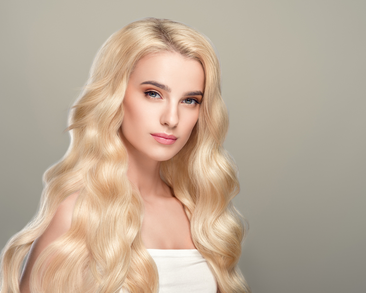 Милая длинноволосая блондинка на сером фоне