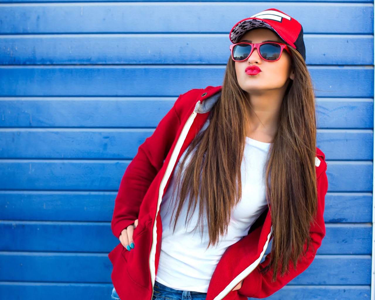 Девушка в бейсболке и солнечных очках у стены