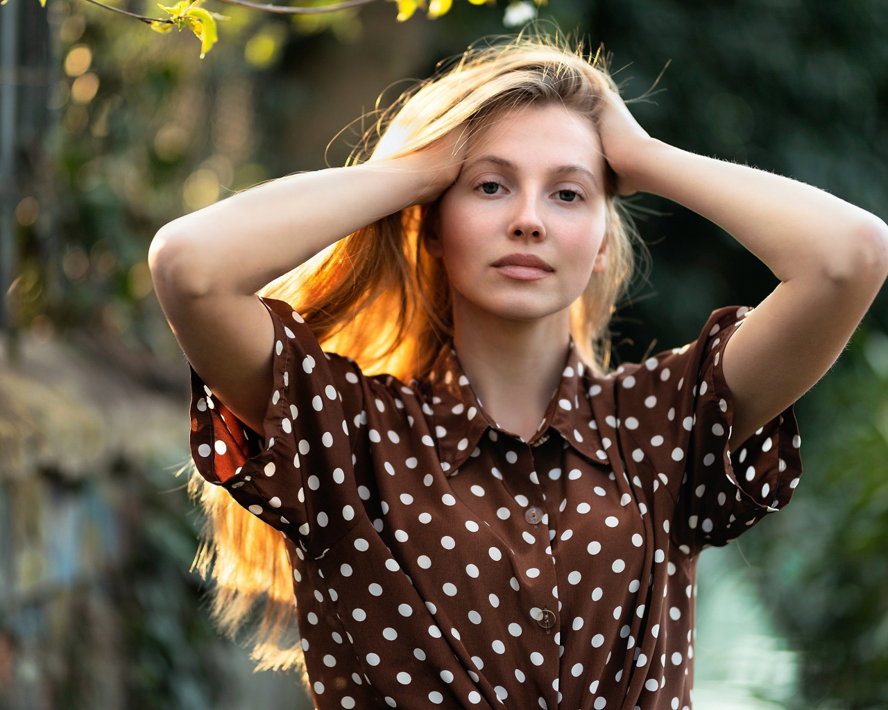 Девушка в рубашке в горох с руками в волосах 