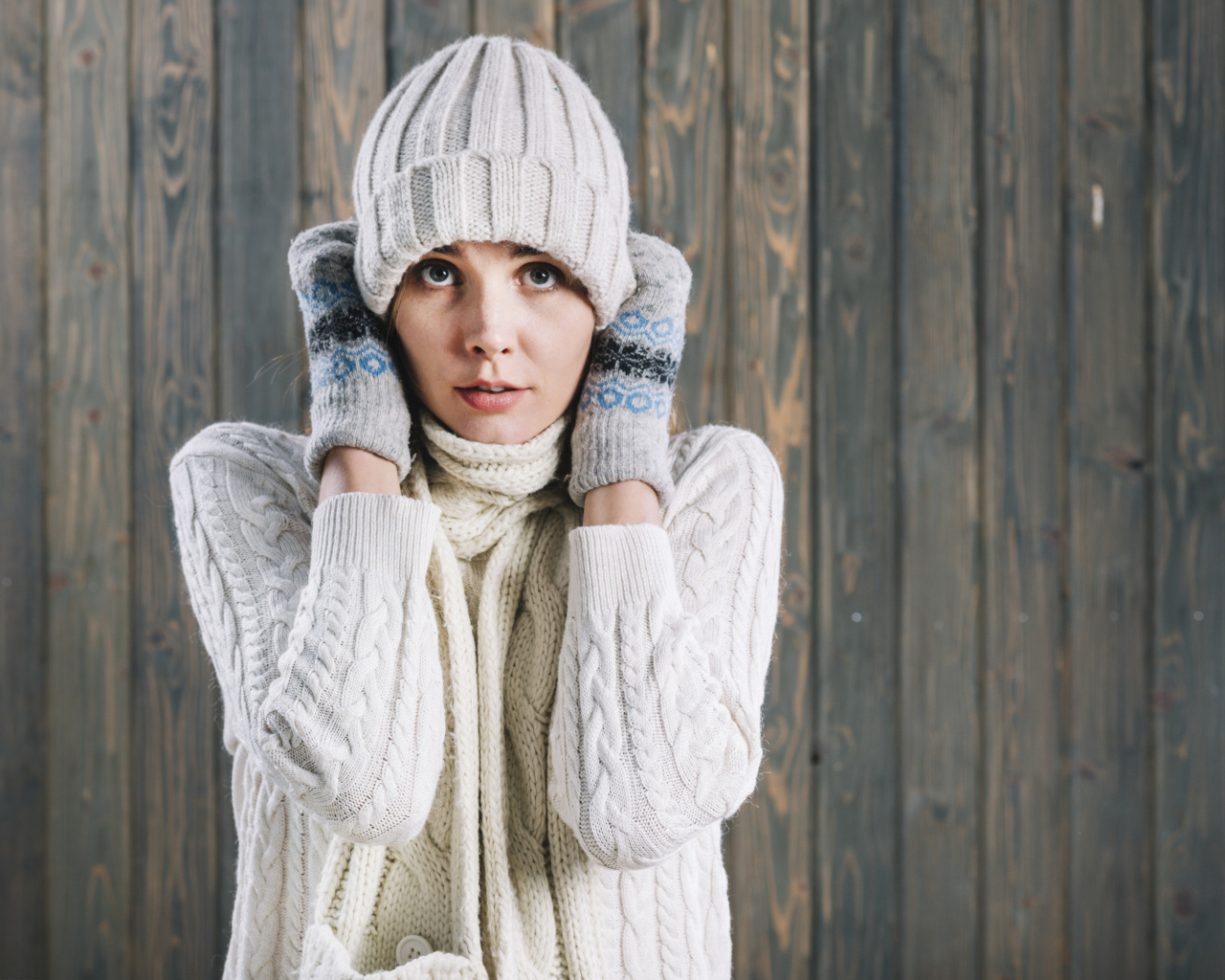 Девушка в варежках поправляет шапку на голове