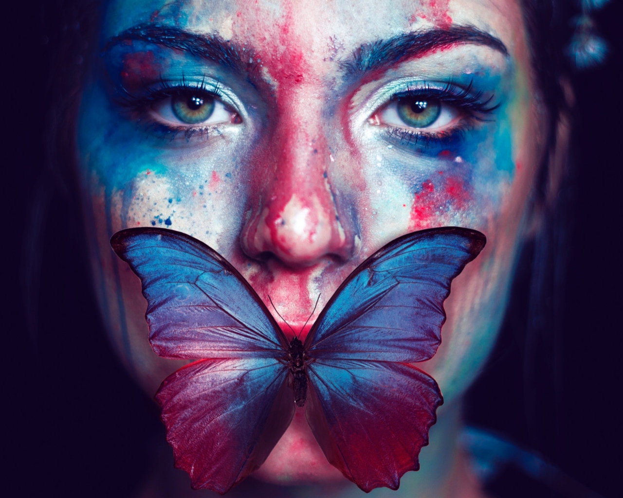 Лицо девушки в краске с бабочкой во рту