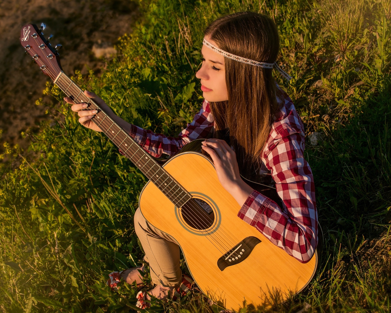 Девушка с гитарой сидит в лучах солнца на траве