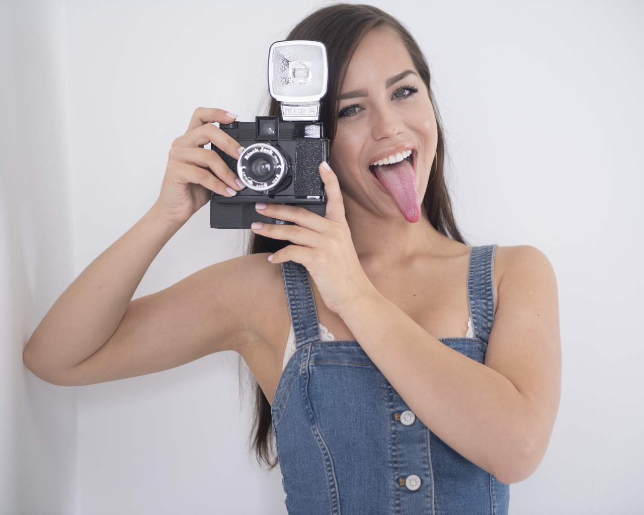 Девушка с высунутым языком с фотоаппаратом в руках