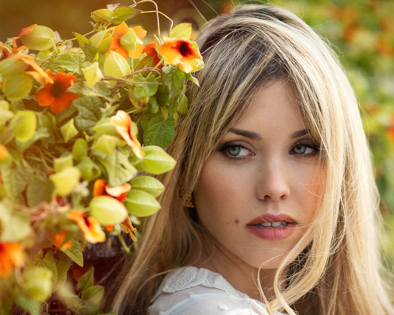 Зеленоглазая блондинка у забора с цветами 