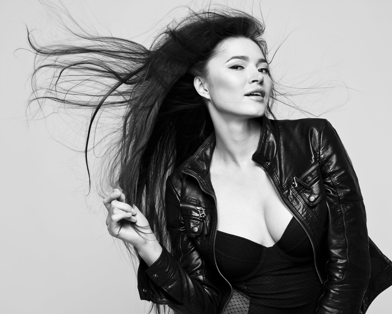 Длинноволосая брюнетка с кожаной куртке на сером фоне