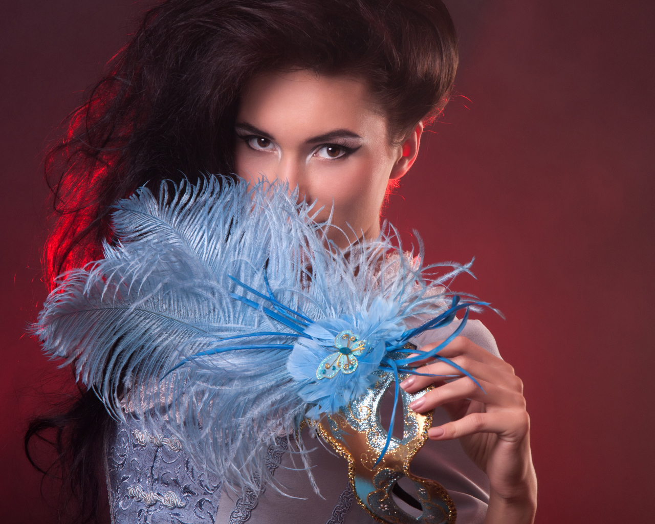 Длинноволосая девушка с маской с перьями в руке