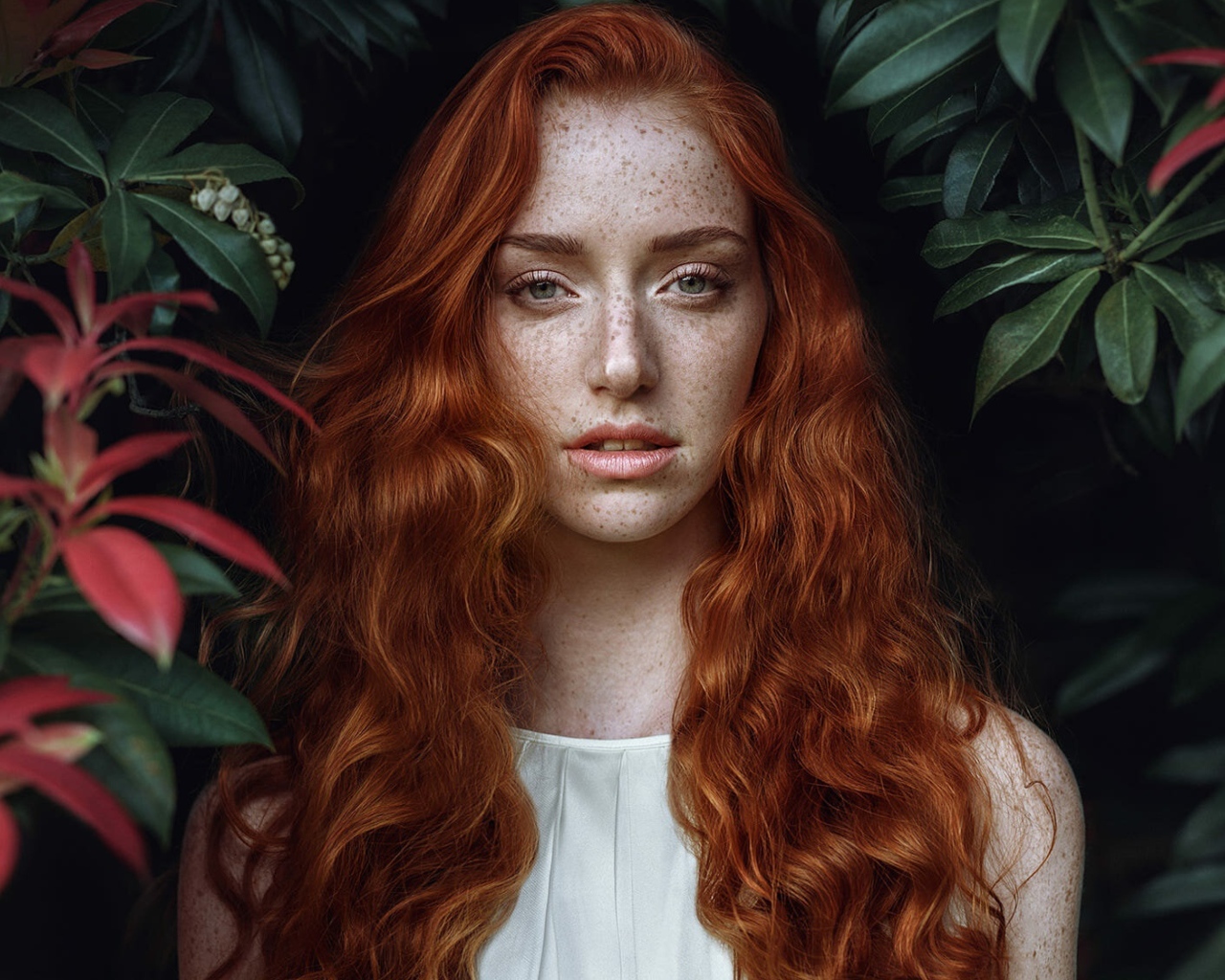 Рыжеволосая девушка с веснушками на лице на фоне кустов 