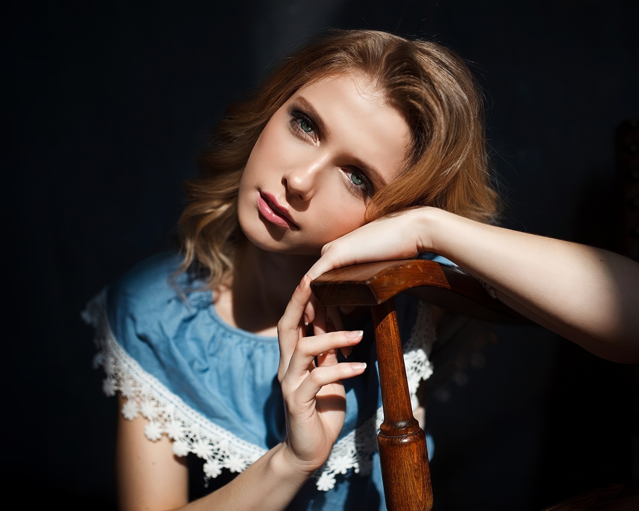 Грустная девушка сидит облокотившись об спинку кресла