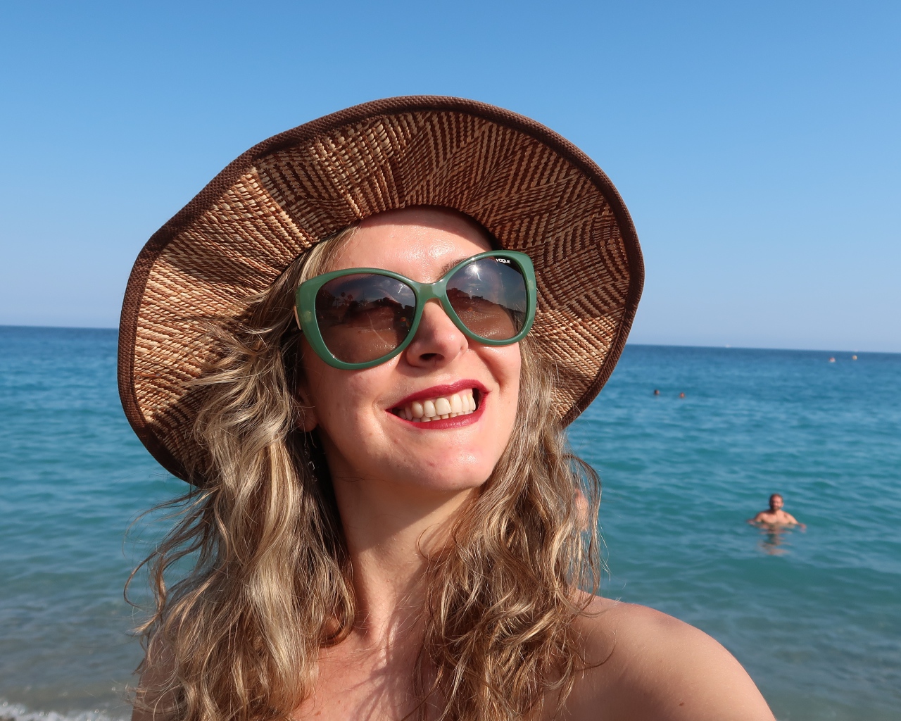 Улыбающаяся девушка в солнечных очках и шляпе на море