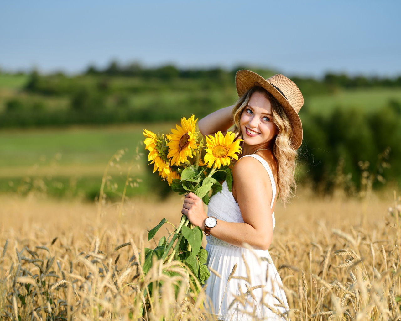 Улыбающаяся девушка на поле с пшеницей с букетом подсолнухов в руке