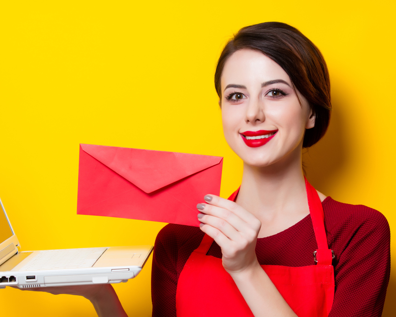 Улыбающаяся девушка с ноутбуком и конвертом в руках на желтом фоне