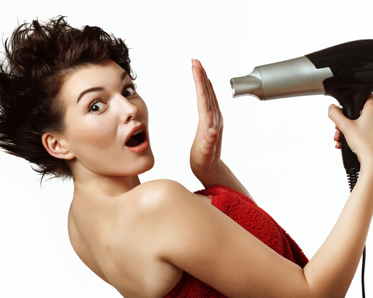 Удивленная девушка с феном в руках на белом фоне