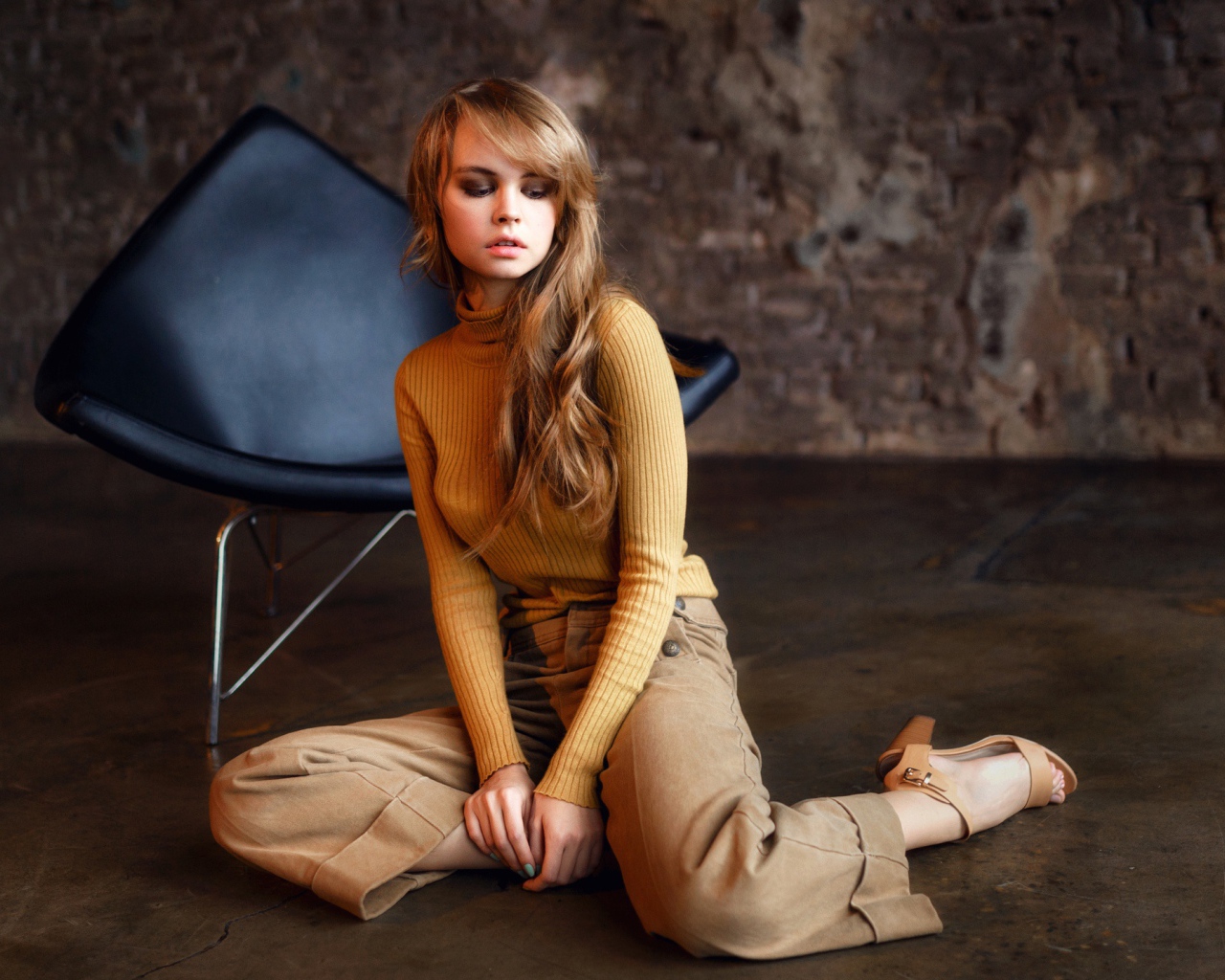 Девушка сидит на полу около черного кресла 