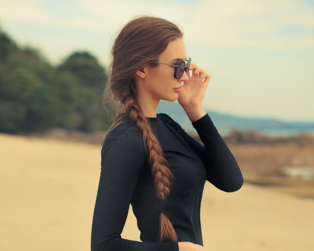Девушка с косой в черных очках смотрит на воду