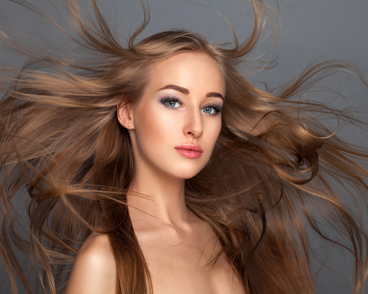 Ветер развивает волосы красивой девушке на сером фоне