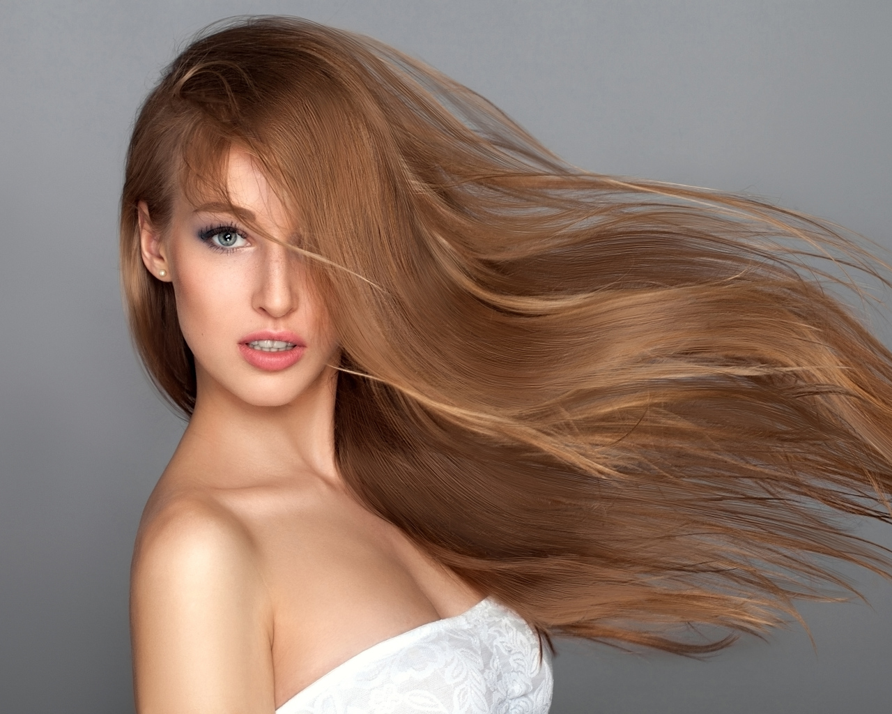 Ветер развивает волосы красивой девушки на сером фоне