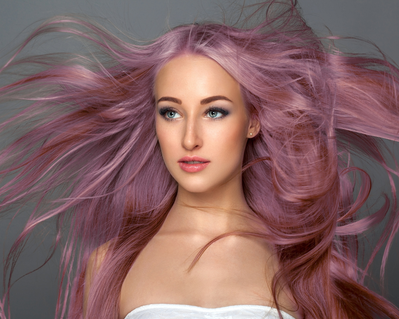 Ветер развивает розовые волосы девушки на сером фоне