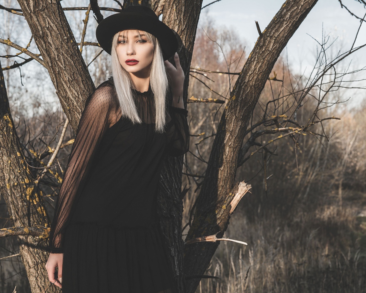 Молодая блондинка в черной шляпе у дерева