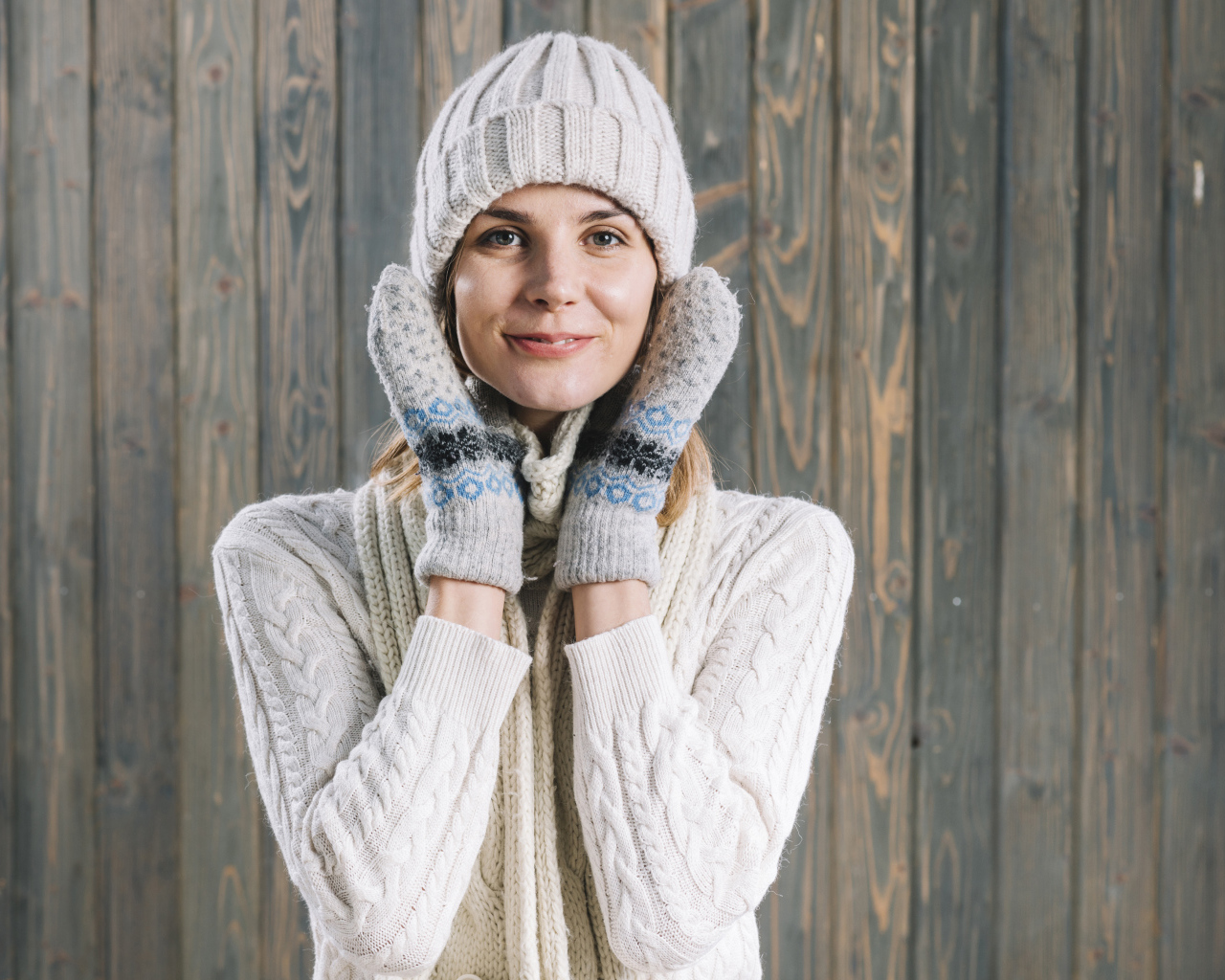 Молодая девушка на шапке, варежках  и теплой шапке на фоне забора