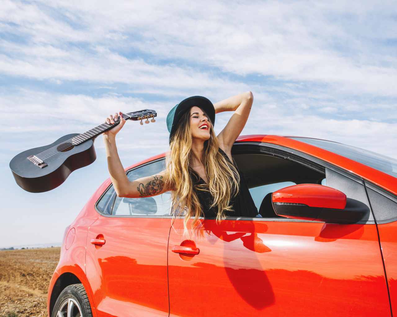 Молодая девушка с гитарой в красной машине летом