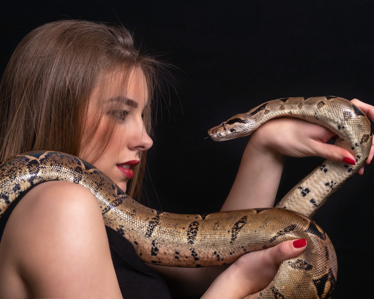 Молодая девушка со змеей в руках на черном фоне