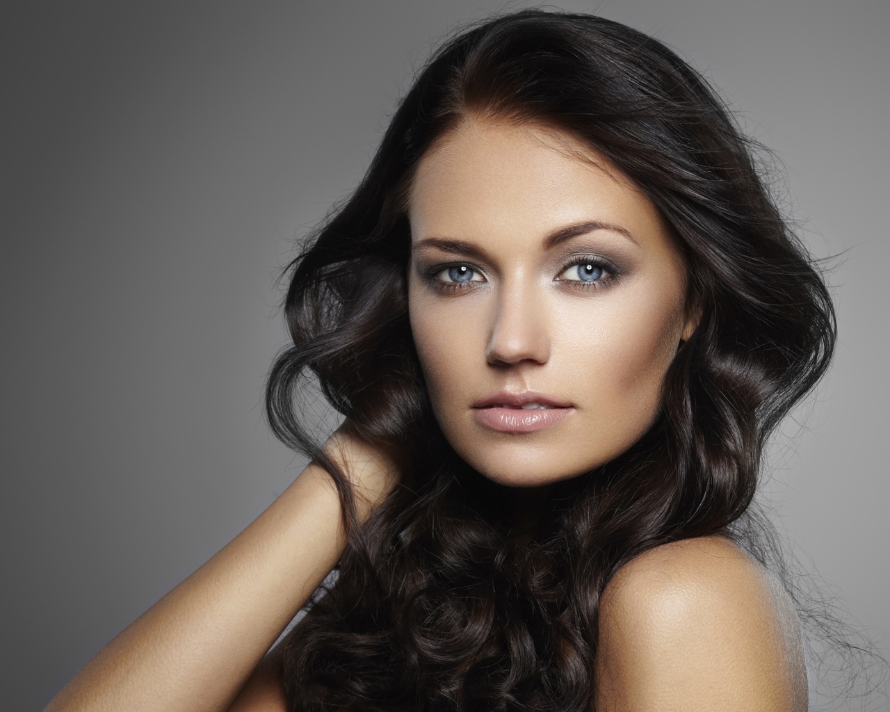 Молодая настоящая голубоглазая длинноволосая брюнетка на сером фоне