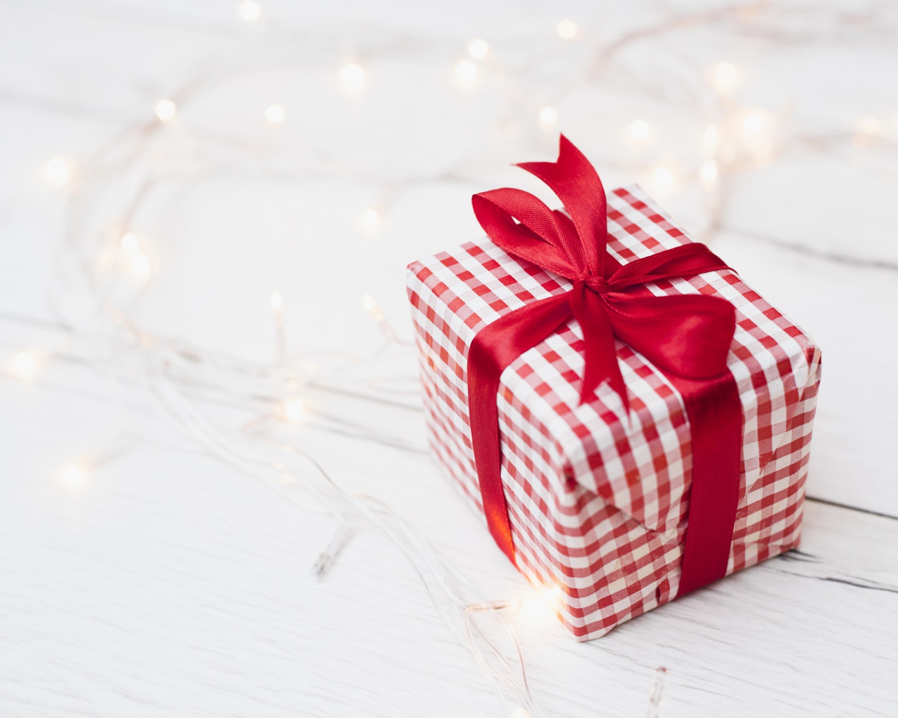 Подарок с красной лентой лежит на столе с гирляндой 