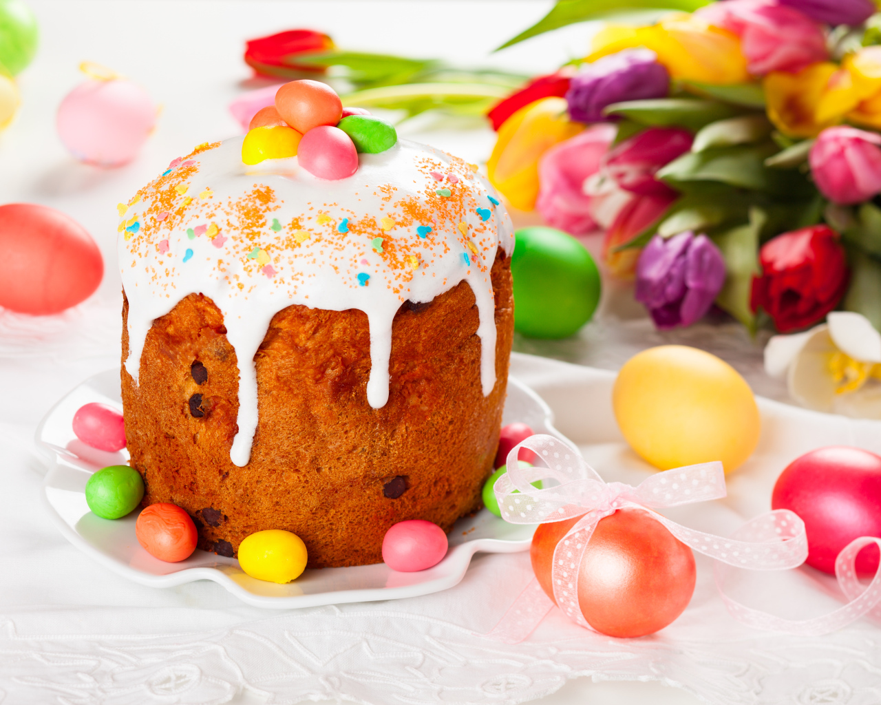 Красивый кулич с конфетами на столе с букетом тюльпанов и крашеными яйцами на Пасху