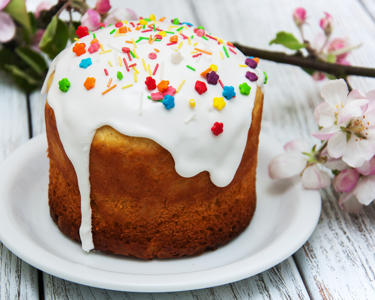 Красивый кулич с белой глазурью на столе с веткой яблони на Великий праздник Пасха