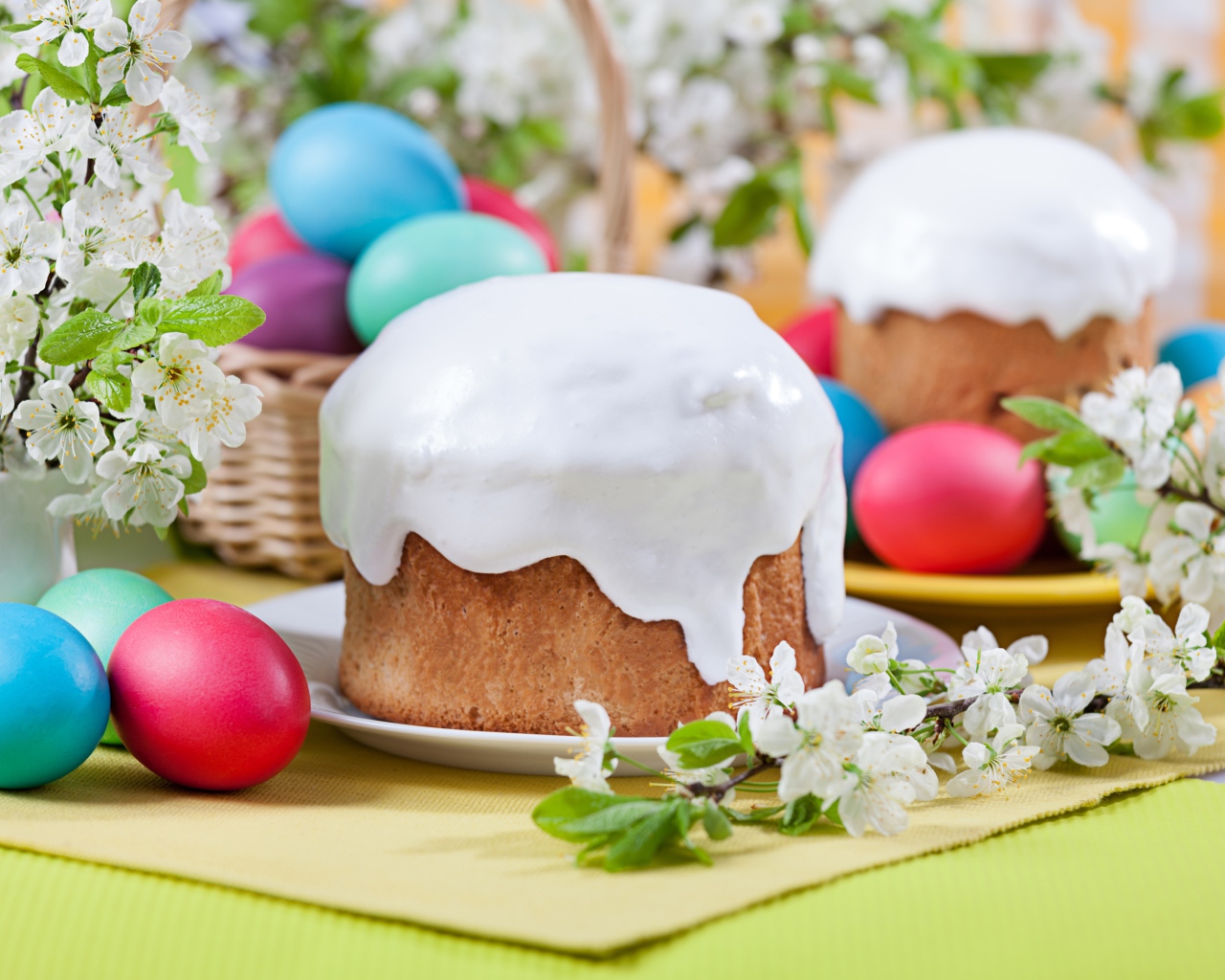 Красивый кулич с белой глазурью на столе с крашеными яйцами и веточками цветущей вишни