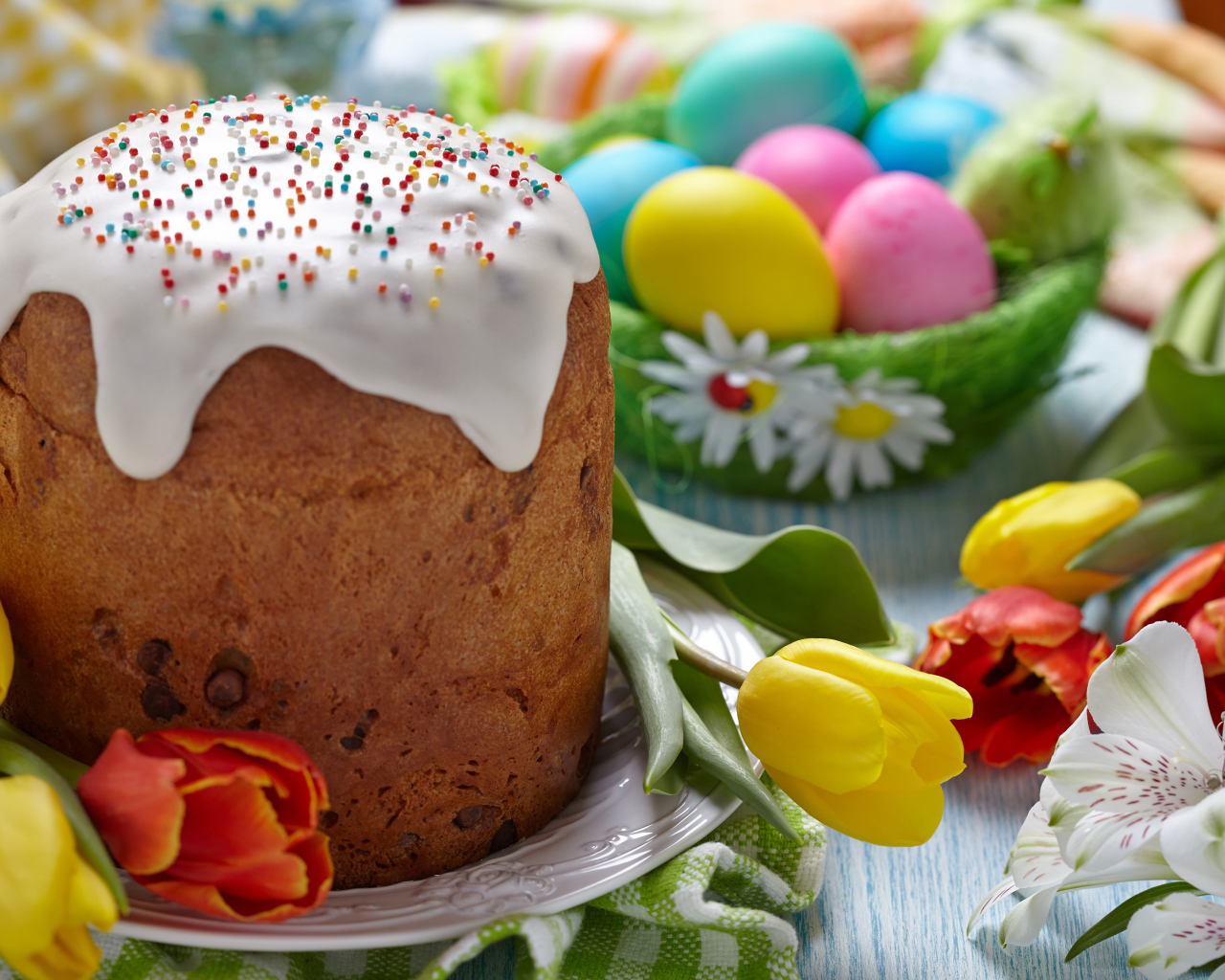 Пасхальный кулич на столе с тюльпанами и крашеными яйцами