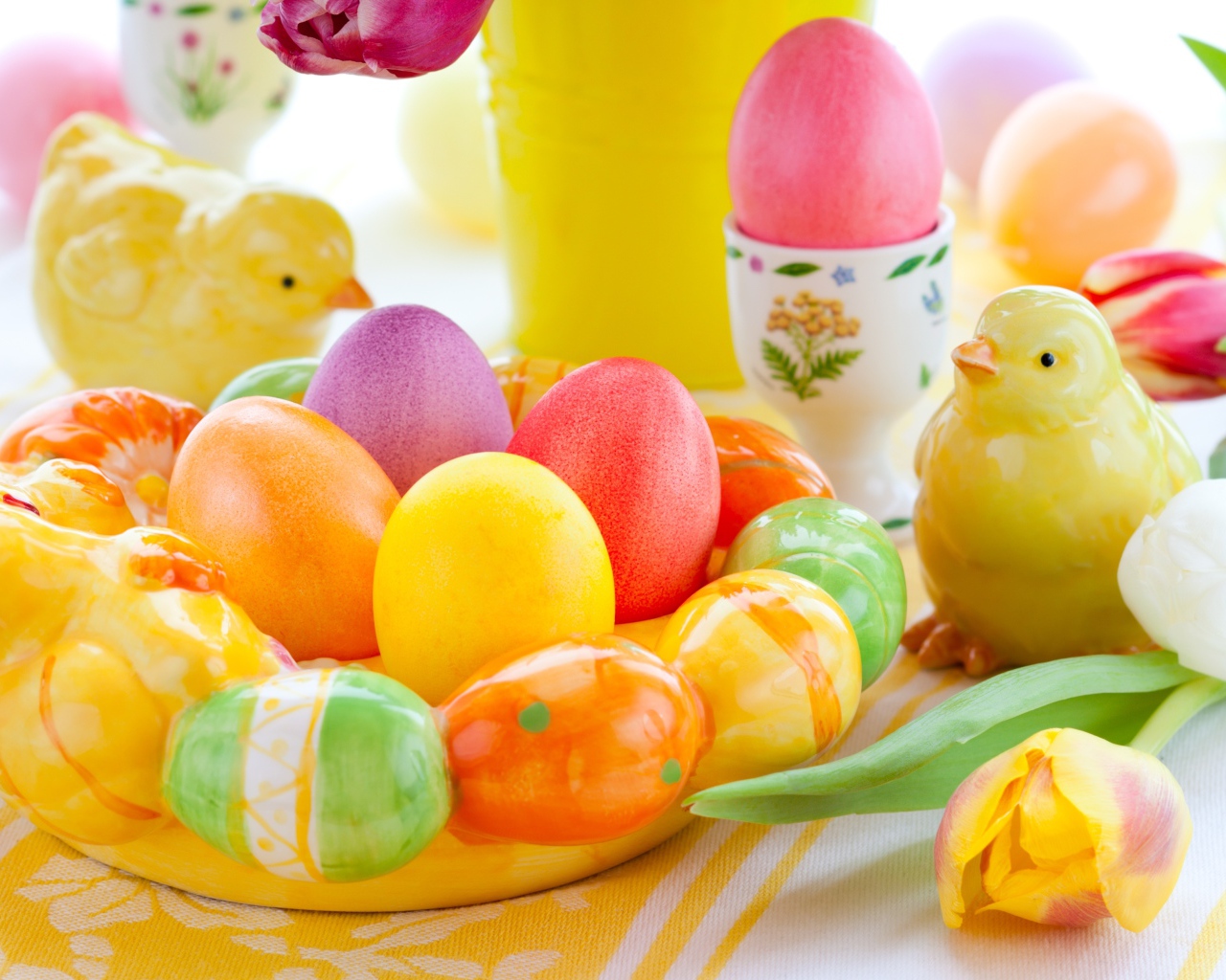 Разноцветные яйца с фигурками на столе с тюльпанами к Пасхе