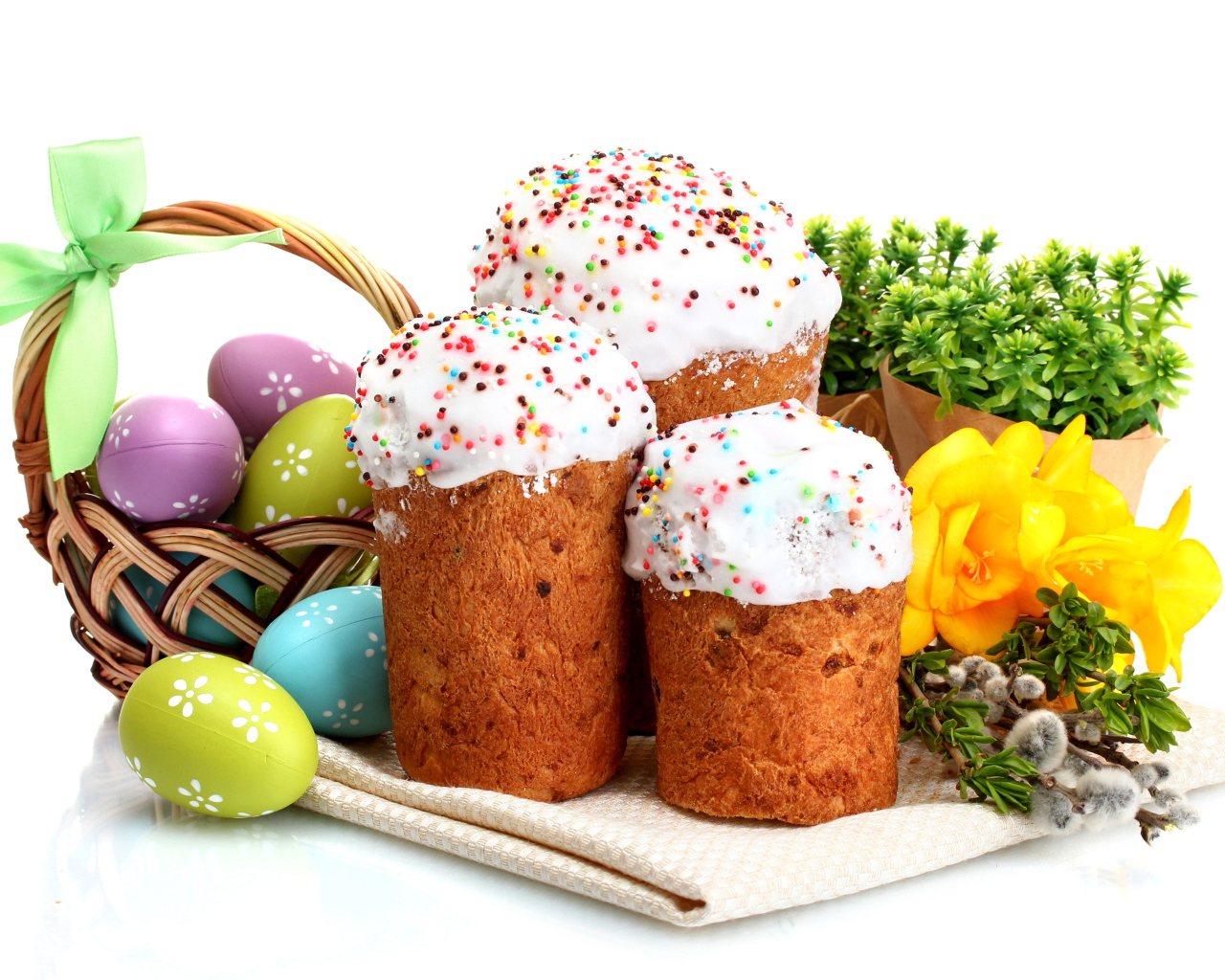 Три сладких кулича на белом фоне с цветами и крашеными яйцами к празднику Пасха