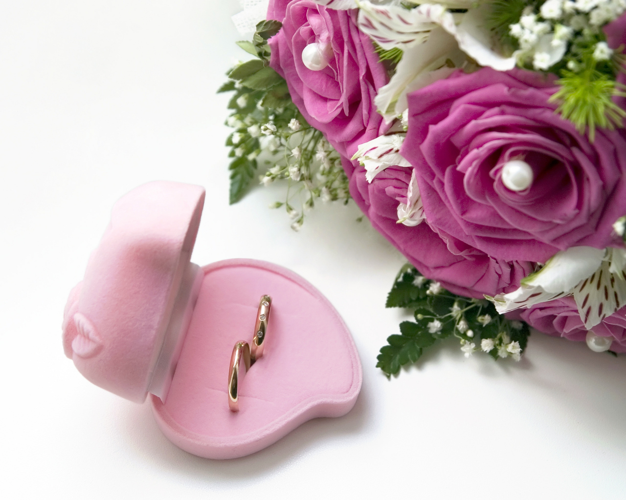 Два обручальных кольца в коробочке на белом фоне с букетом роз