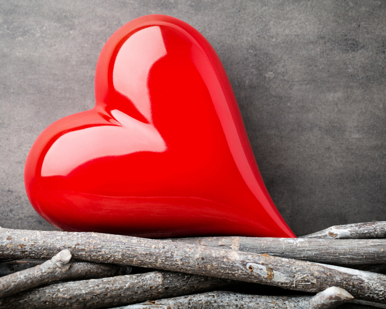 Большое красное сердце лежит на ветках на фоне серой стены