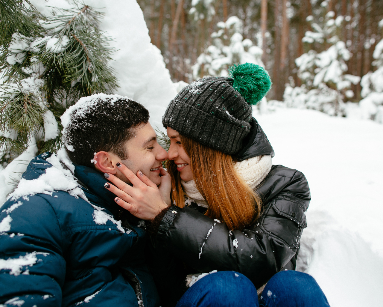 Влюбленная пара сидит под заснеженной еловой веткой зимой