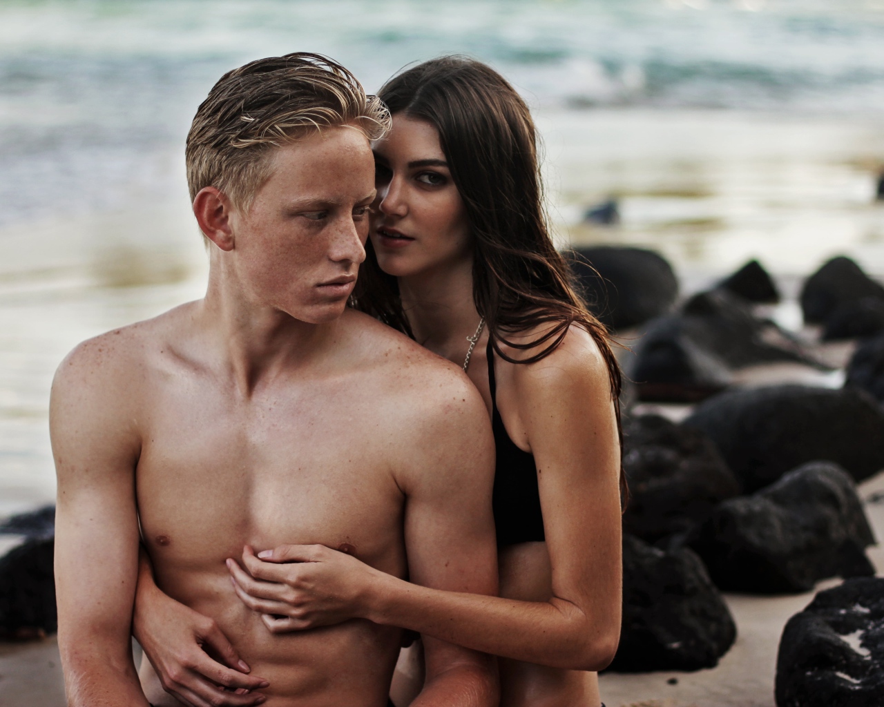 Влюбленная пара сидит на камнях на берегу моря 