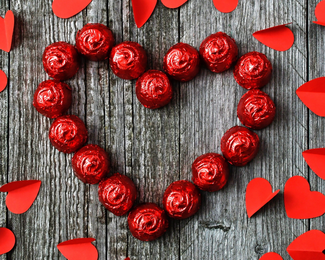 Красное сердце из конфет на деревянном фоне с бумажными сердечками
