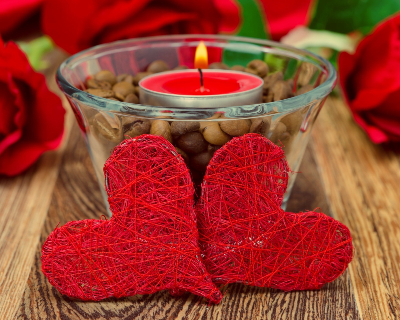 Два красных плетеных сердца на столе с зажженной свечой