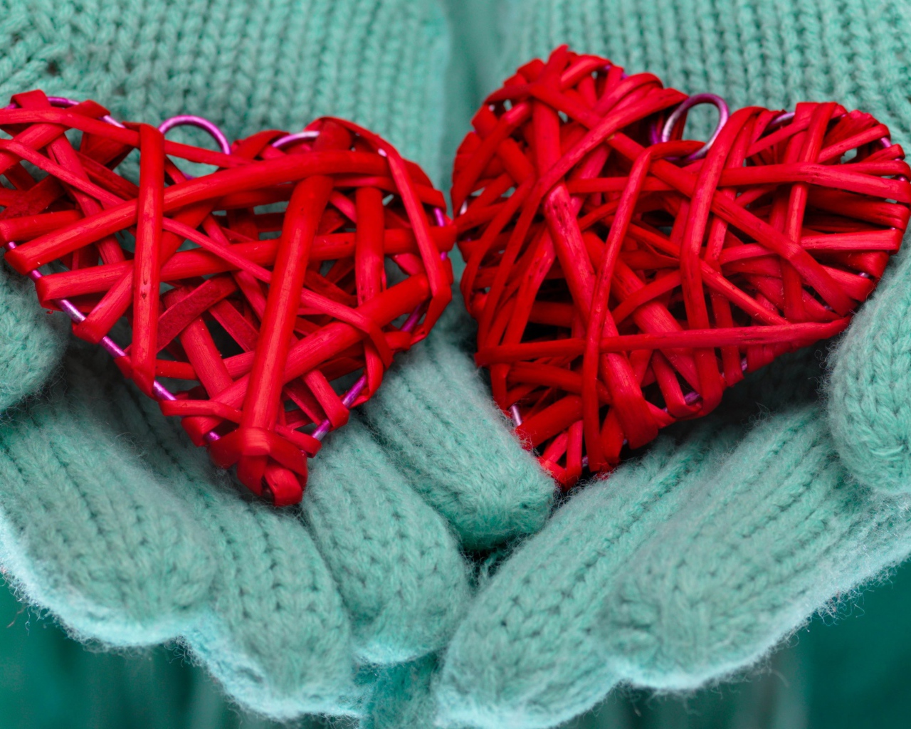Два плетеных красных сердца лежать на руках в варежках