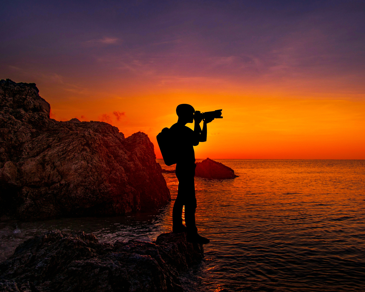 Мужчина фотографирует закат на берегу моря