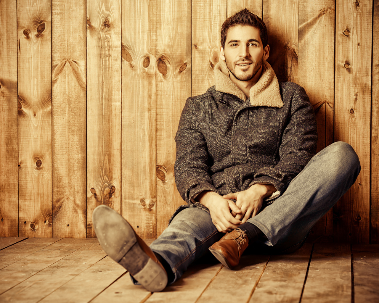 Молодой мужчина в пальто сидит у стены