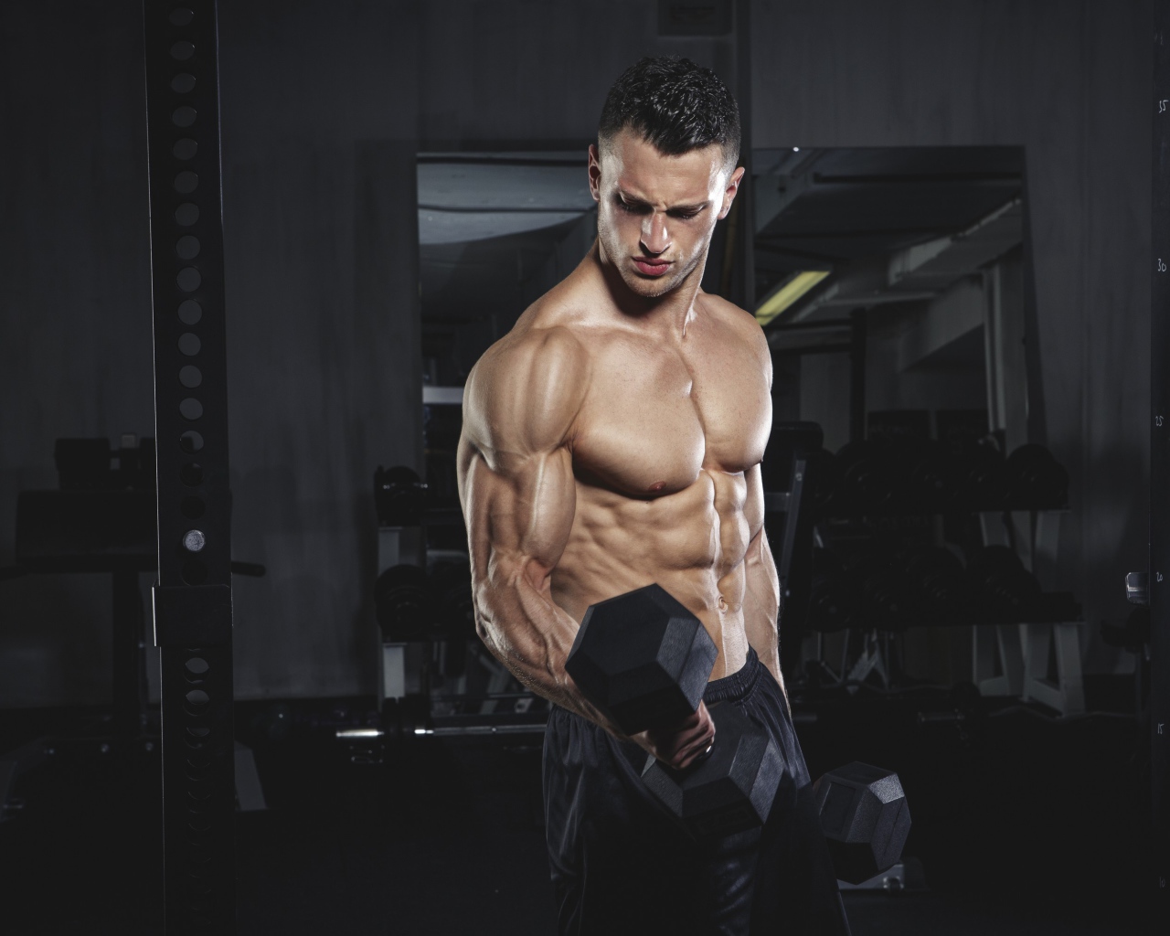 Накаченный мужчина с тяжелыми гантелями в руках 