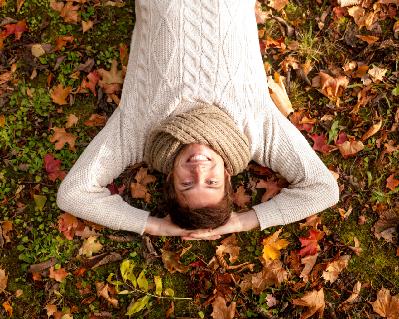 Улыбающийся мужчина в свитере лежит на опавших листьях 